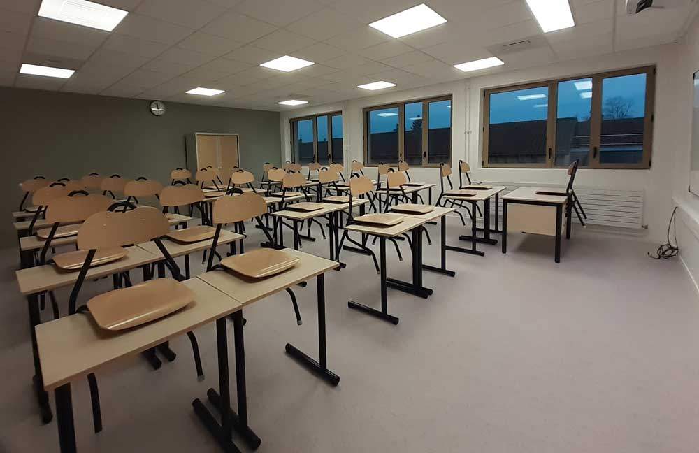 Salle de classe avec des bureaux et des chaises posées dessus