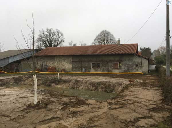 Chantier de création d un site de rétention d'eau : trou dans la terre au premier plan et maison ancienne en arrière plan